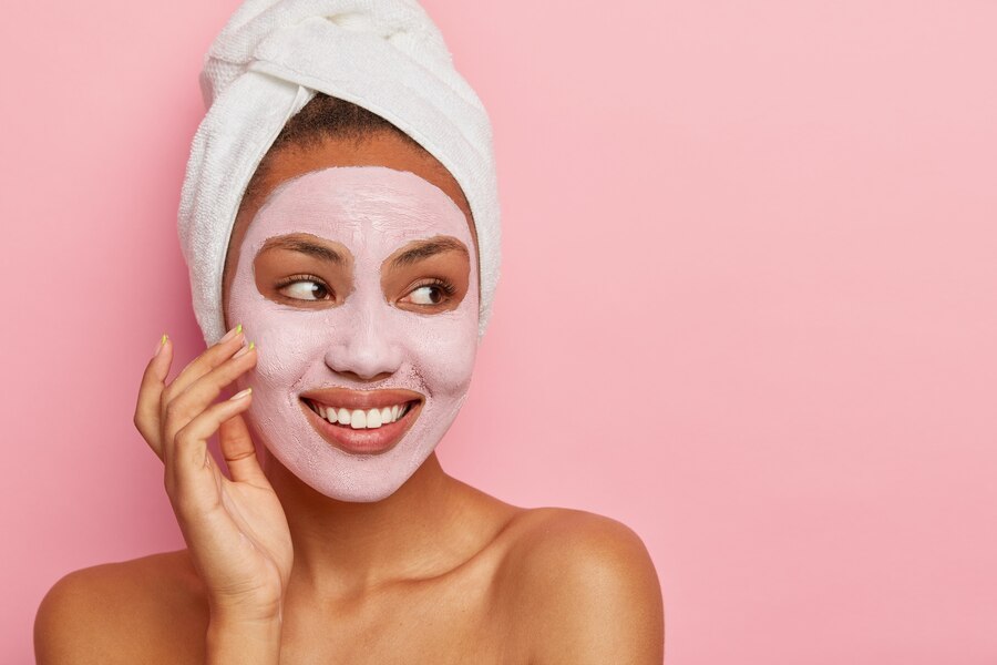 lovely woman has delicate sooth skin wears cream mask face reduce acnes has healthy complexion hygienic treatments wears white wrapped towel head