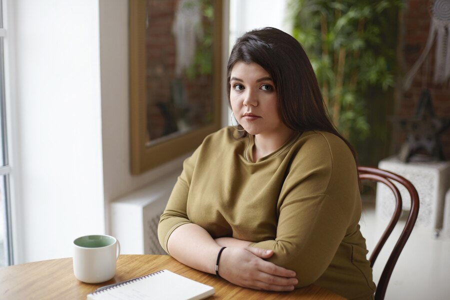 attractive-young-overweight-chubby-woman-having-coffee-sitting-cafe-with-mug-copybook-table-staring-with-serious-look-making-important-notes-diary-planning-sketching_344912-2513