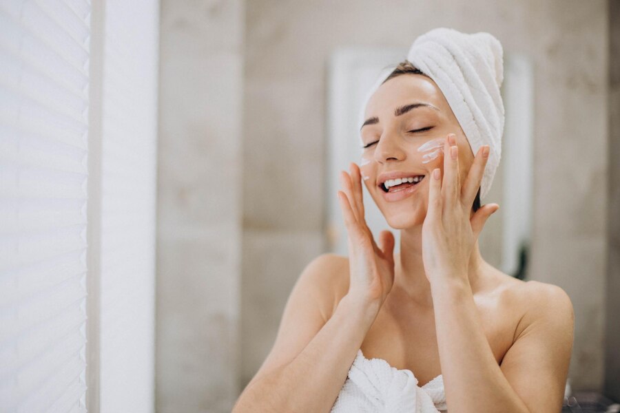 young-woman-applying-face-cream-her-face-with-towel-head_1303-30535