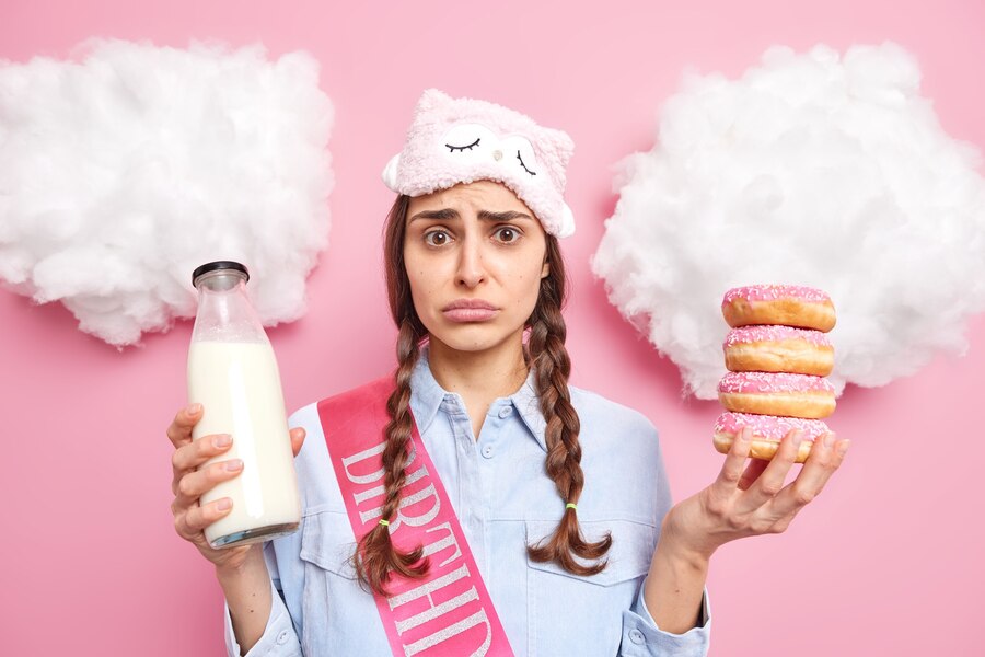 girl-has-pigtails-looks-with-sulking-expression-wants-eat-baked-delicious-doughnuts-eats-sweet-dessert-drinks-fresh-milk-wears-casual-clothes-isolated-pink_273609-49091