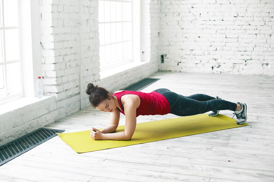 people-sports-fitness-strength-endurance-concept-stylish-brunette-athletic-girl-sportswear-exercising-spacious-hall-by-window-doing-elbow-plank-green-yoga-mat-wooden-floor_344912-1068