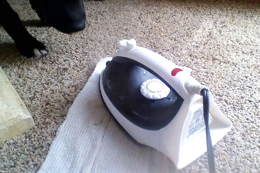 What type of stains can be removed using iron and towel on carpet