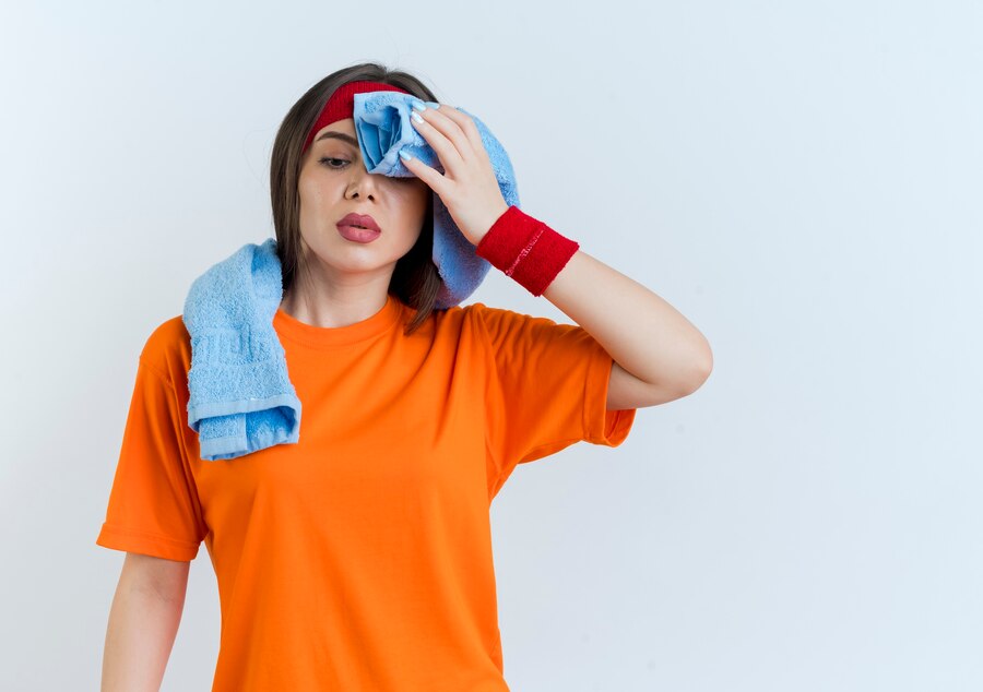 tired young sporty woman wearing headband wristbands with towel around neck looking down wiping sweat with towel  