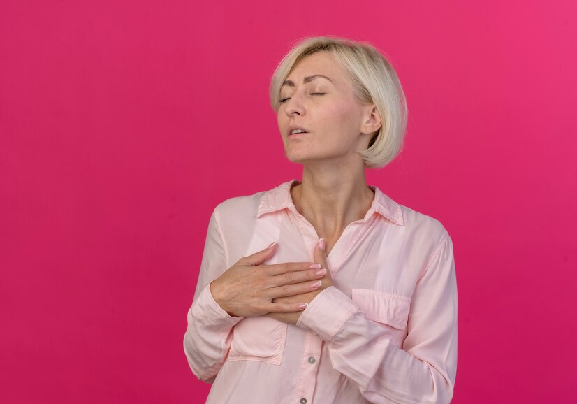 peaceful young blonde slavic woman keeping hands chest with closed eyes isolated pink background with copy space  